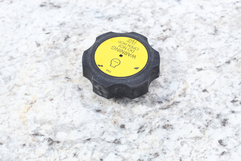 Black radiator cap with yellow warning label.